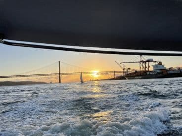 A stunning sunset view from a boat, showcasing a sailboat in the foreground and a bridge in the background — perfect for capturing the beauty of a sailing adventure.