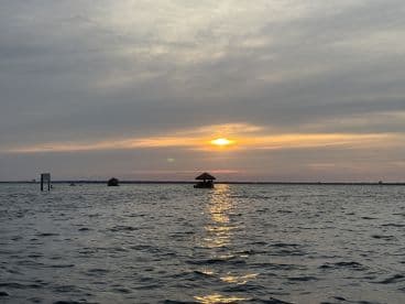 A serene sunset view over the water, featuring a tranquil scene with huts in the distance — perfect for capturing the beauty of evening boat rides.
