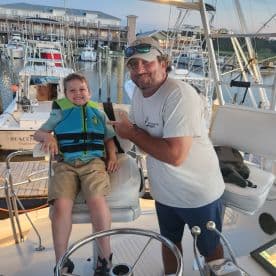 A joyful moment aboard a boat as a child in a life jacket poses with an adult, capturing the essence of family fun on the water.