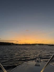 A serene sunset view from the bow of a boat, showcasing the tranquil waters and distant shoreline — perfect for evening cruises and relaxation on the water.