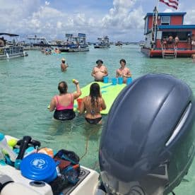 A lively group enjoys a fun day at the sandbar, playing games and swimming in the clear waters — the perfect setting for a summer party on the water.