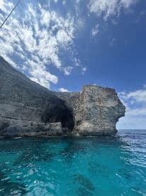 A stunning view of a rocky coastline with a cave, showcasing the vibrant turquoise waters and dramatic sky — perfect for adventure seekers exploring coastal landscapes.