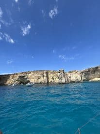A stunning view of a rocky coastline with sailboats anchored nearby, showcasing the beauty of the open water and perfect for sailing adventures.
