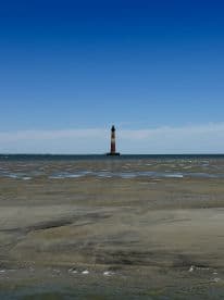 A stunning view of a lighthouse standing tall against a clear blue sky, surrounded by tidal flats — a perfect representation of coastal beauty and maritime heritage.