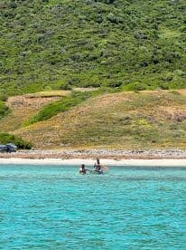 Two friends enjoy paddleboarding in crystal-clear waters near a sandy beach, perfect for summer adventures and water activities.