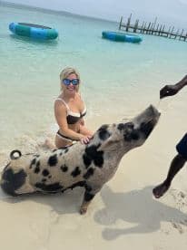 A woman interacts with a friendly pig in shallow waters, showcasing a unique wildlife experience in the Bahamas.