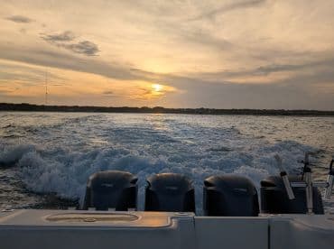 A stunning sunset view from the back of a boat, showcasing the powerful engines and the wake as it cruises through the water.
