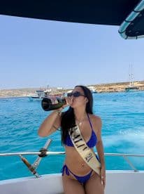 A woman in a bikini celebrates on a boat, enjoying champagne against a stunning turquoise backdrop — perfect for party vibes and summer fun.