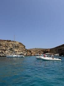 A lively scene featuring multiple boats anchored near a stunning coastline, with guests enjoying the sun and water activities — perfect for a summer adventure.