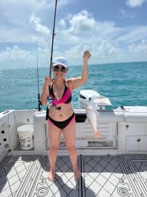 A woman proudly displays her catch while fishing on a boat in the open ocean, showcasing the excitement of a day on the water.