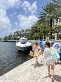 A lively group walks along the dock towards a boat, surrounded by palm trees and a vibrant waterfront scene — perfect for a day of adventure on the water.