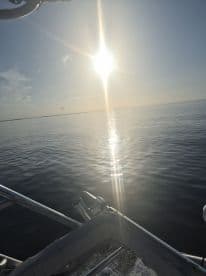 A serene view of the sun reflecting on calm waters, showcasing the boat's structure in the foreground — perfect for capturing tranquil moments on the water.