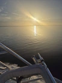 A serene sunset view from the bow of a boat, showcasing calm waters and a beautiful sky — perfect for evening cruises.