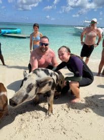 A group interacts with a friendly pig on the beach, showcasing a unique wildlife experience in the Bahamas — perfect for animal lovers and adventure seekers.