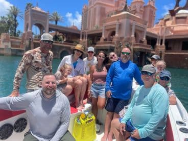 A cheerful group of friends and family gather on a boat, enjoying a sunny day out on the water, with a stunning backdrop of tropical architecture.
