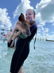 A young girl joyfully holds a pig while wading in shallow waters, showcasing a unique wildlife interaction in a tropical setting.