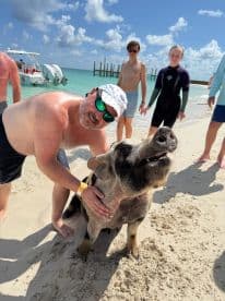 A joyful interaction between a man and a friendly pig on the beach, with children enjoying the unique wildlife experience — a memorable moment in the Bahamas.