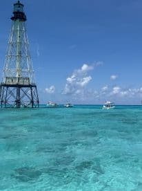 A stunning view of a lighthouse surrounded by turquoise waters, with boats navigating nearby — a picturesque scene perfect for boating adventures.