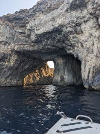 A stunning view of a natural rock formation with an arch, seen from a boat, showcasing the beautiful coastline and inviting waters perfect for exploration.