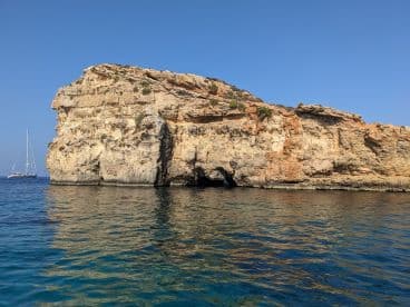 A stunning view of a rocky coastline with a sailboat in the distance, perfect for showcasing the natural beauty of sailing adventures.