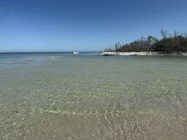 A serene view of a clear coastline with a boat anchored in the distance, showcasing the beauty of a tranquil beach setting.