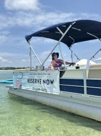 A cheerful woman enjoys a sunny day aboard a pontoon boat, inviting guests to reserve their adventure. Perfect for family outings or group fun on the water.