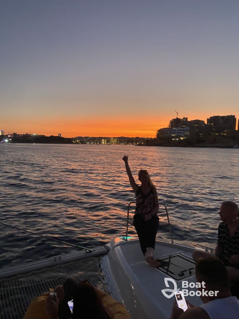 A lively group enjoys a stunning sunset aboard a catamaran, capturing the perfect moment of celebration on the water.
