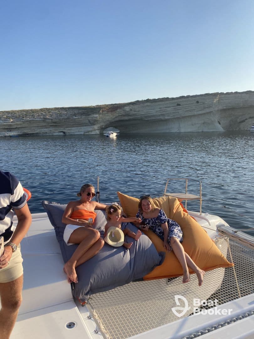 A joyful family enjoys a relaxing moment on a catamaran, lounging on oversized cushions with stunning coastal views in the background — perfect for memorable summer outings.
