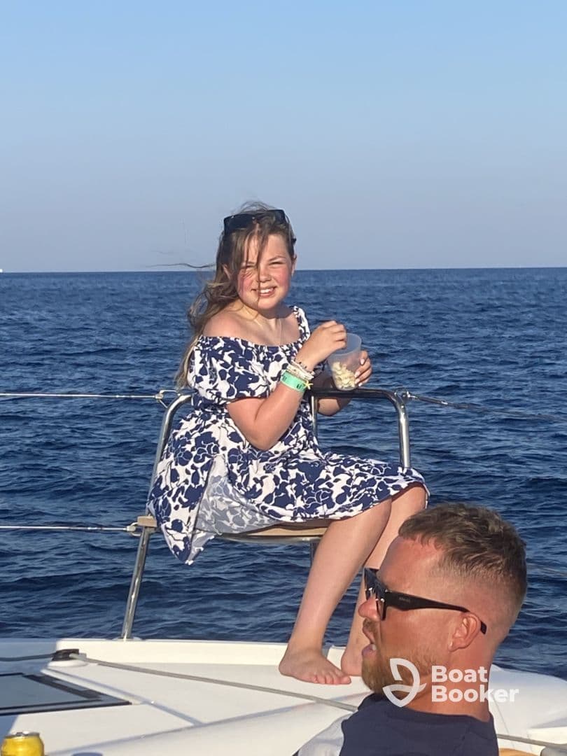 A young girl enjoys a snack while sitting on the edge of a boat, capturing a joyful moment on the water — perfect for family outings and summer adventures.
