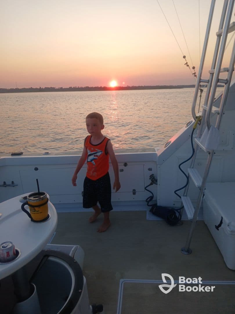 A child stands on the deck of a boat during a beautiful sunset, capturing a memorable family moment on the water.