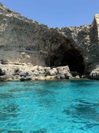 A stunning view of a rocky coastline and cave entrance, surrounded by crystal-clear turquoise waters — a perfect destination for exploration and adventure.