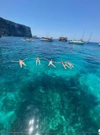 A group of friends enjoys a refreshing swim in the crystal-clear waters, surrounded by boats and stunning coastal scenery — perfect for a summer getaway.