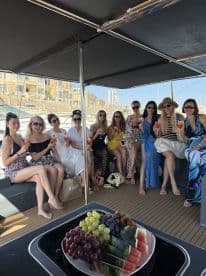 A lively group of friends celebrates aboard a yacht with cocktails and a beautiful spread of fresh fruit, perfect for a bachelorette party or summer getaway.