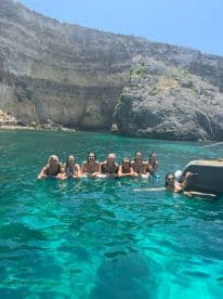 A group of friends enjoys a refreshing swim in crystal-clear waters, surrounded by stunning cliffs — perfect for summer adventures and memorable outings.