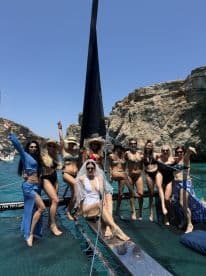 A lively group of women celebrates a bachelorette party aboard a yacht, showcasing fun and camaraderie against a stunning coastal backdrop.