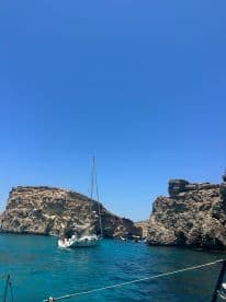 A picturesque sailboat navigates through crystal-clear waters near stunning rocky cliffs, showcasing the beauty of a coastal adventure.