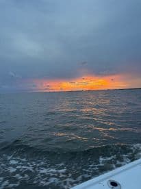 A serene sunset view over the water, captured from a boat, showcasing the tranquil beauty of the evening sky reflecting on the waves.