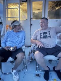 Two men relax in the cabin of a boat, enjoying a conversation in a cozy seating area — perfect for unwinding during a fishing trip or cruise.