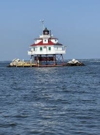 A picturesque lighthouse stands on stilts over calm waters, showcasing a classic design and serving as a charming landmark in the landscape.