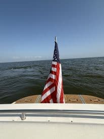 A striking view of a boat's stern featuring an American flag, set against a clear blue sky and calm waters — perfect for showcasing nautical pride.