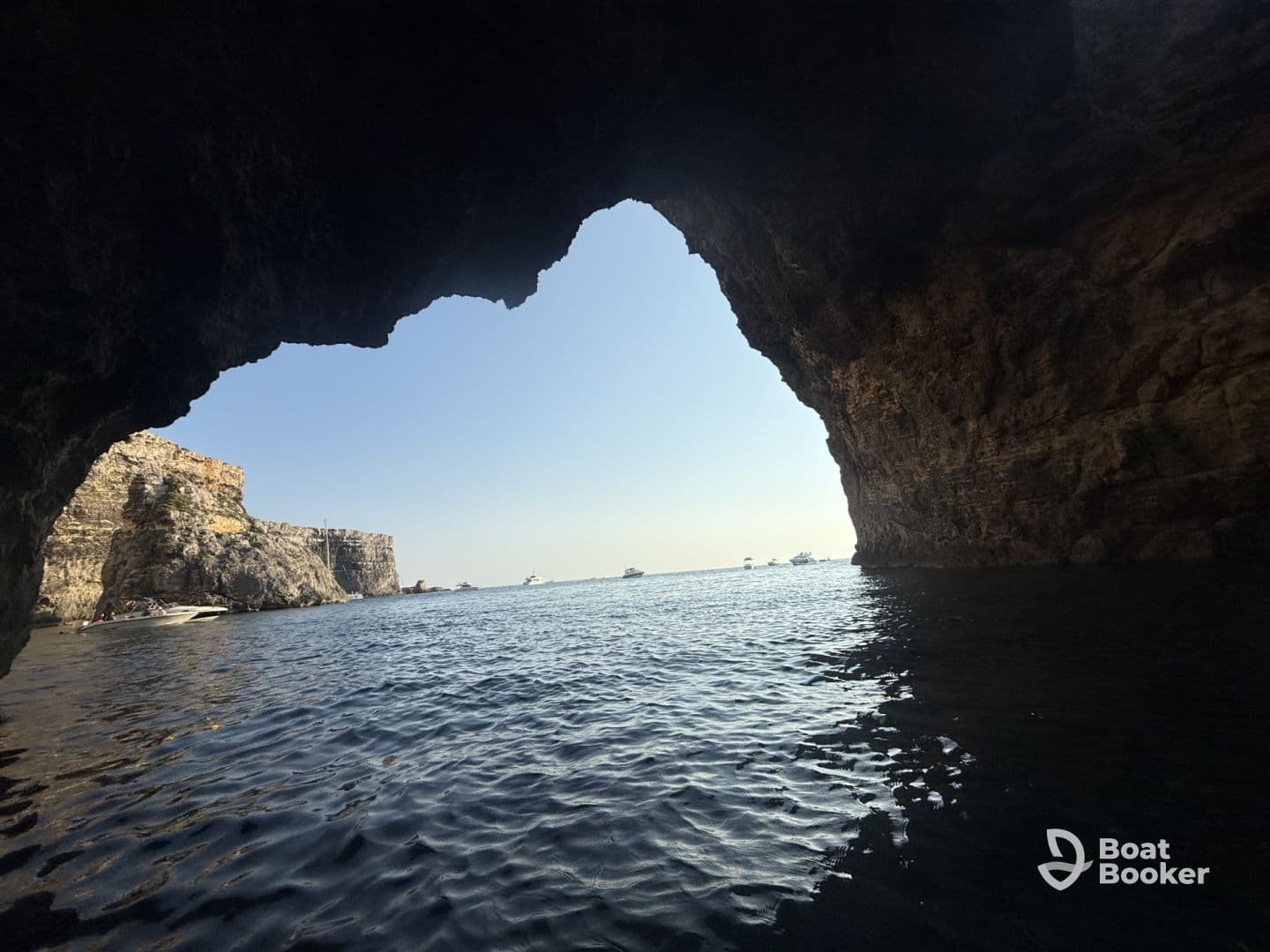 A stunning view from inside a cave, showcasing the serene waters and boats outside — a perfect spot for exploring coastal wonders.