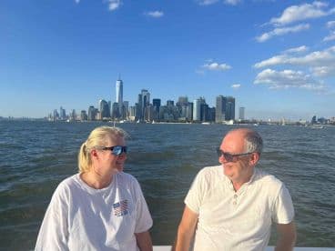 A couple enjoys a scenic boat ride with the stunning New York City skyline in the background, perfect for sightseeing and romantic outings on the water.