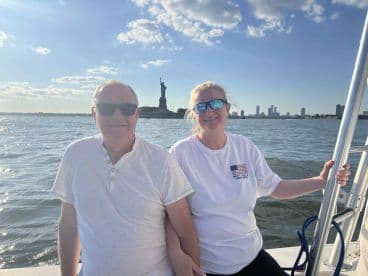 A couple enjoys a scenic boat ride with the Statue of Liberty in the background, capturing a memorable moment against the stunning New York City skyline.