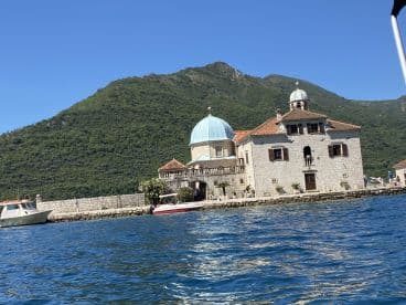 A picturesque view of a historic waterfront building set against lush green mountains, showcasing the beauty of the landscape and the charm of the location.