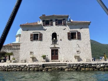 A picturesque view of a historic stone building along the waterfront, with visitors enjoying the scenic surroundings — a perfect spot for sightseeing and capturing memories.
