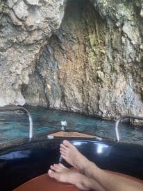 A serene moment captured inside a cave with clear waters, showcasing a person's feet resting on the boat — a perfect escape into nature's beauty.