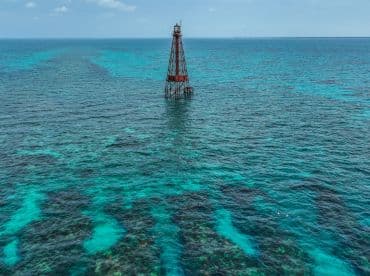 A stunning aerial view of a lighthouse surrounded by vibrant turquoise waters, with snorkelers exploring the area — a perfect destination for marine adventures.