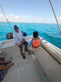 A joyful moment on a fishing trip, featuring a man and a child enjoying their time on a boat in vibrant turquoise waters.