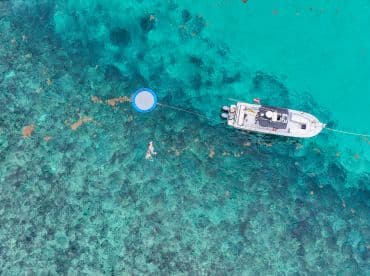 An aerial view captures a person swimming near a boat in crystal-clear waters, showcasing a perfect day for water activities and relaxation.