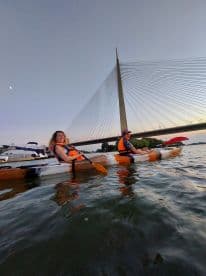 A couple enjoys a scenic kayaking experience at sunset, with a stunning bridge in the background — perfect for adventure seekers and nature lovers.